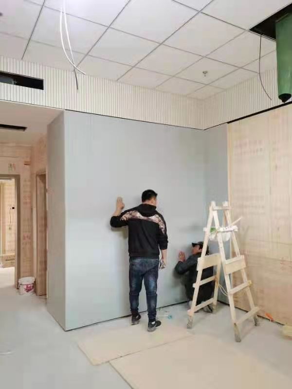 办案区审讯室灰色防撞软包墙板现场安装施工,工人将高密度海绵软包固定于墙面,防自伤防撞处理