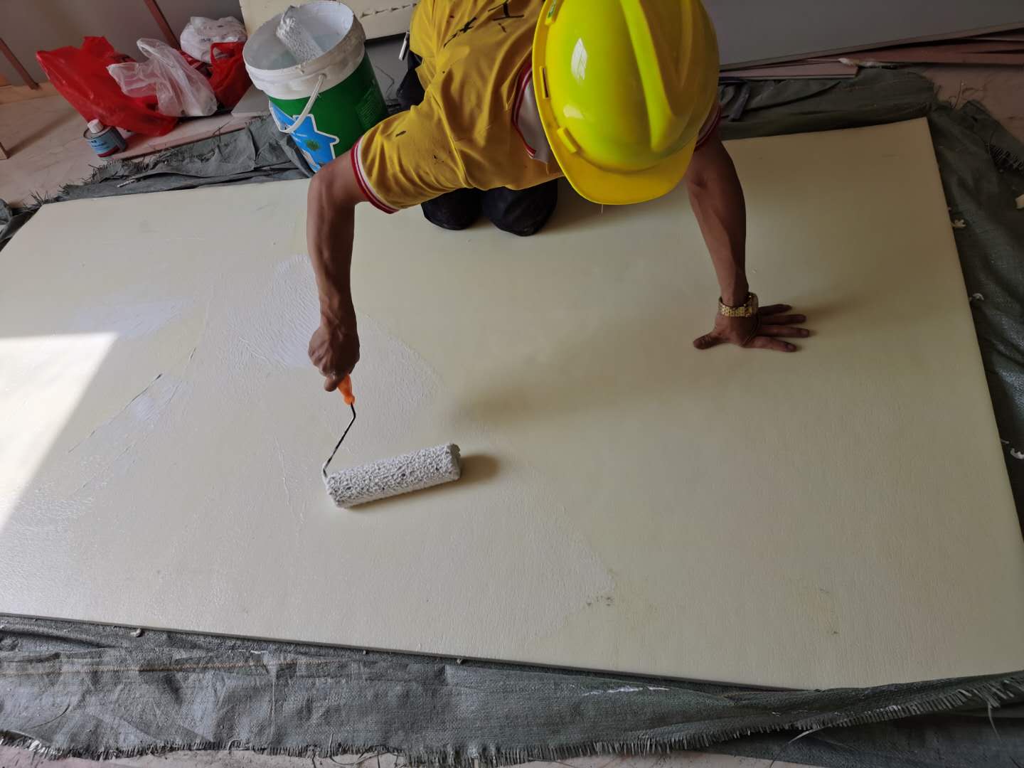 工人戴安全帽用滚筒在大幅防撞软包背面滚涂胶粘剂,防撞软包安装施工现场实景