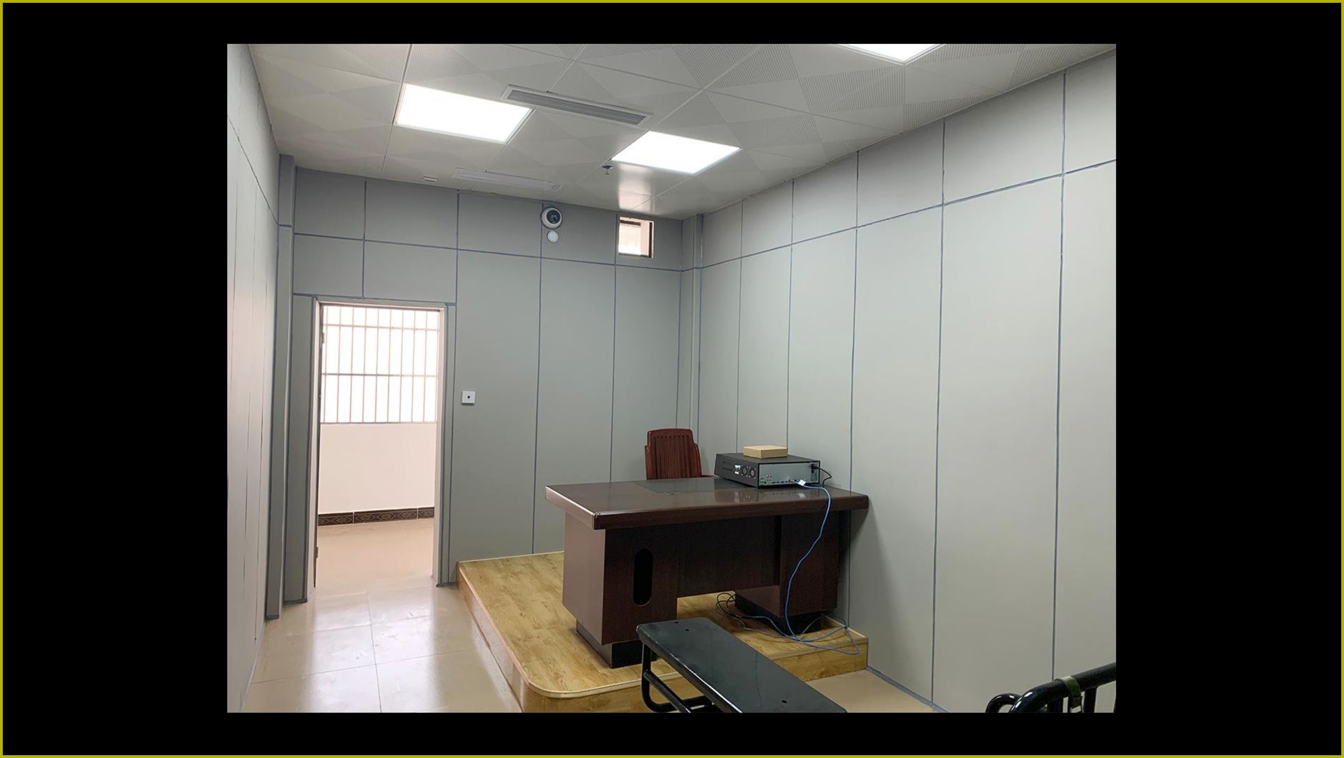 公安办案区审讯室防撞软包墙面整体装修实景,灰色软包墙板满铺搭配审讯桌椅