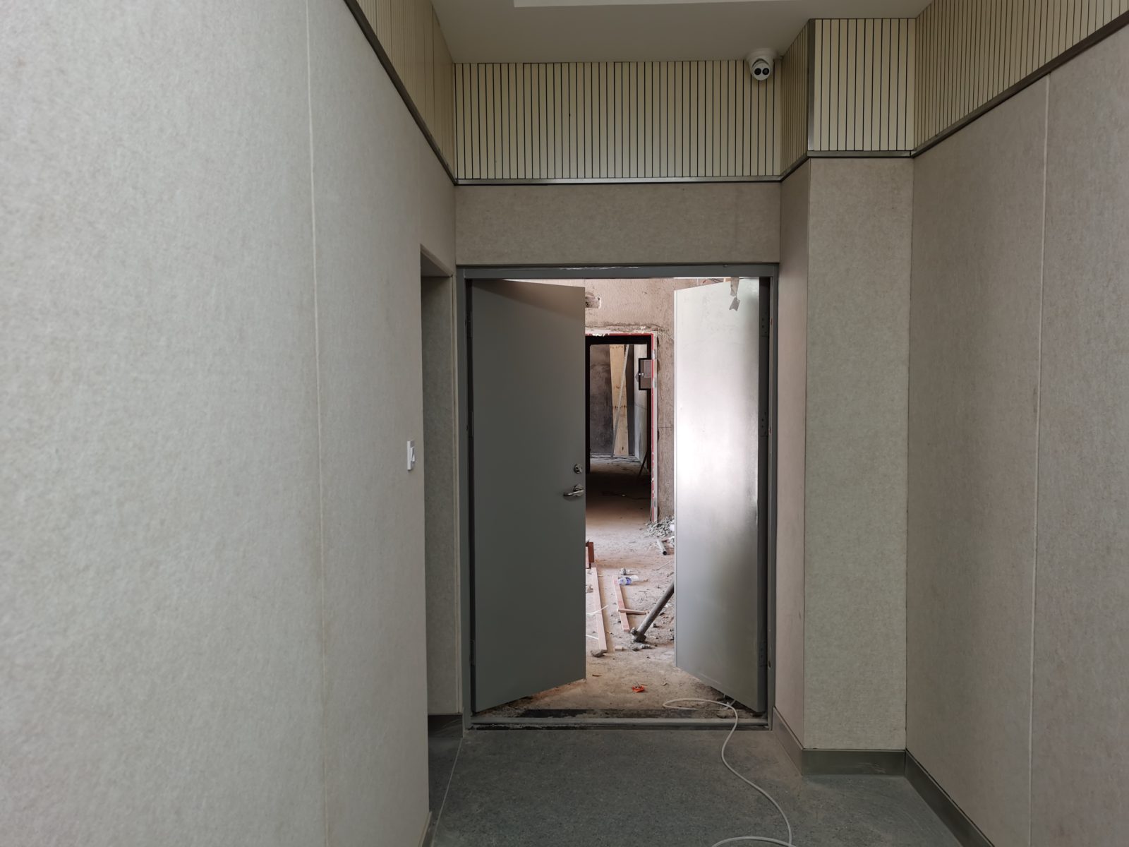 办案区审讯室灰色防撞软包墙面与钢制防撞门安装实景,上方搭配米色木条吸音板,防自伤防撞设计