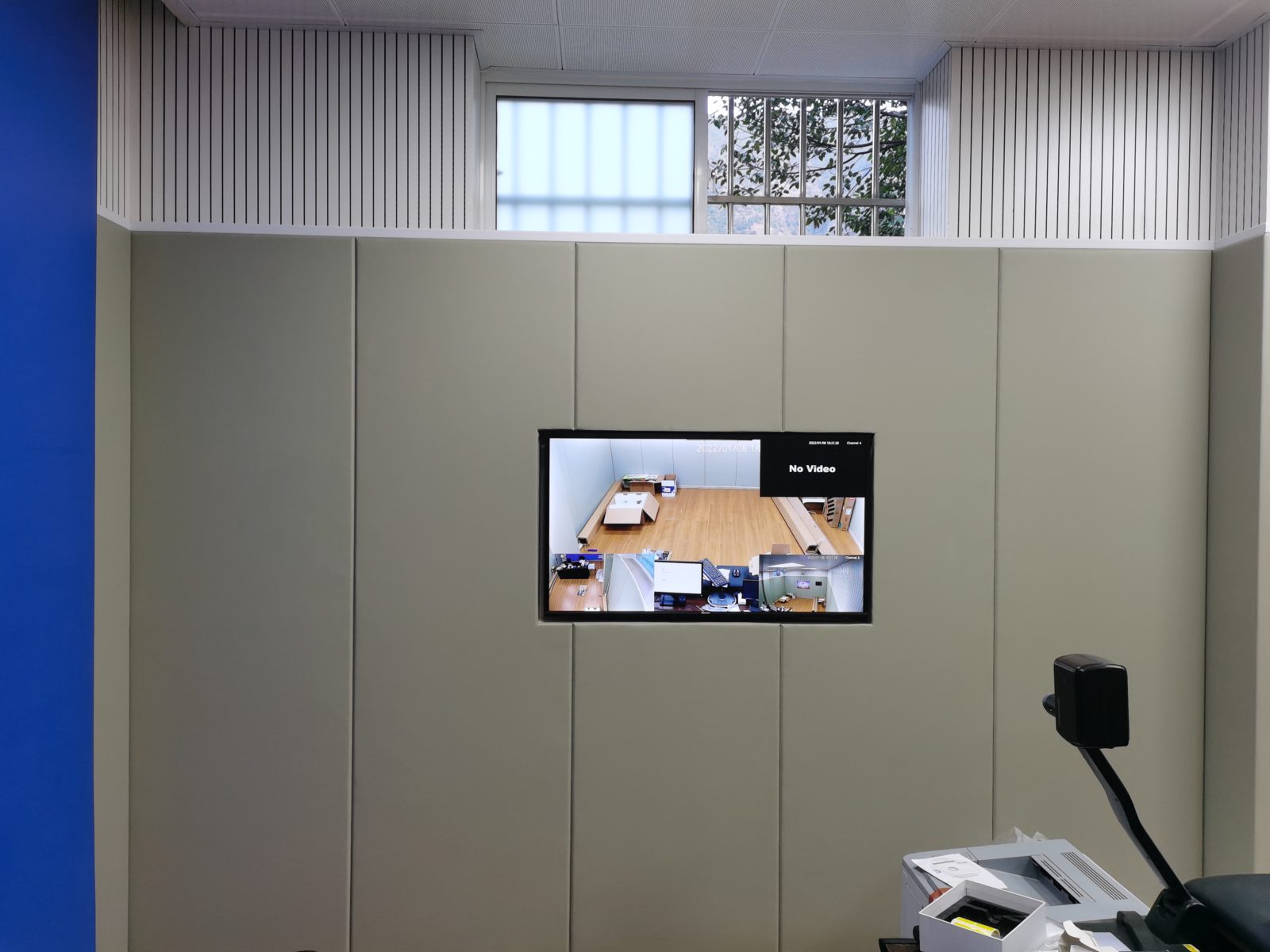 公检法办案区审讯室米色防撞软包墙面装修实景,嵌入监控显示屏,上部搭配白色木条吸音板防自伤设计