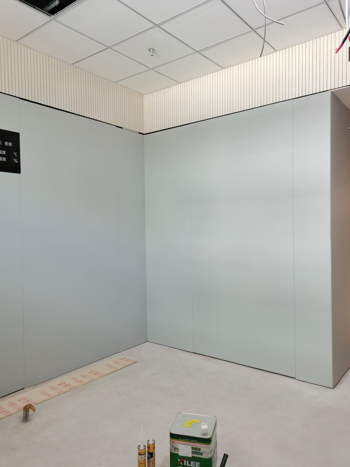 办案区审讯室灰色防撞软包墙面安装实景,顶部搭配木条吸音板与矿棉板吊顶